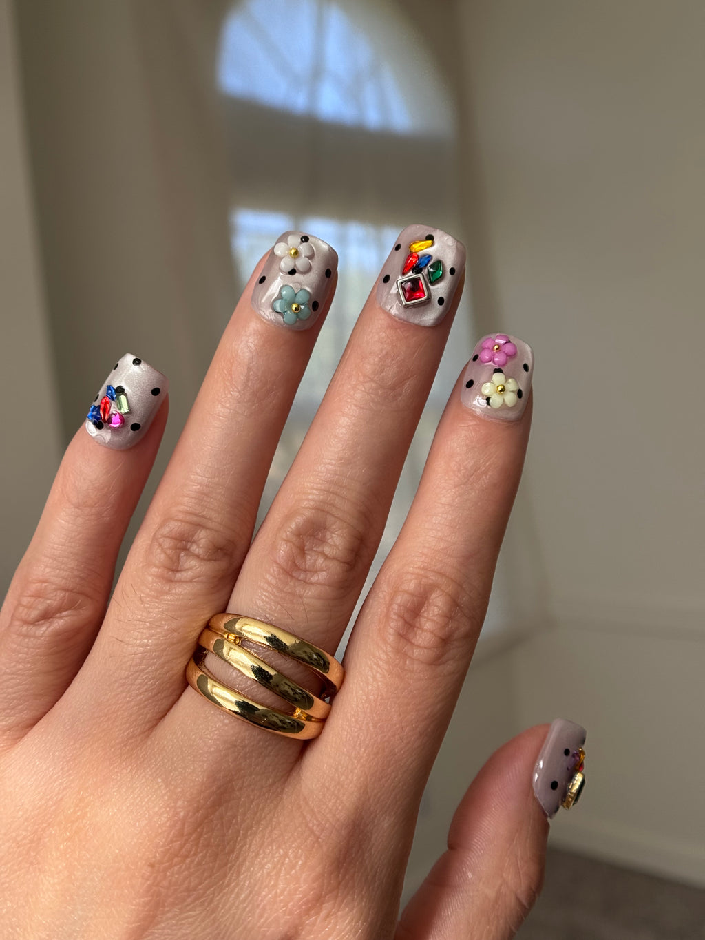 A close-up of a hand showcasing a set of colorful nail art designs with rhinestones and floral patterns.