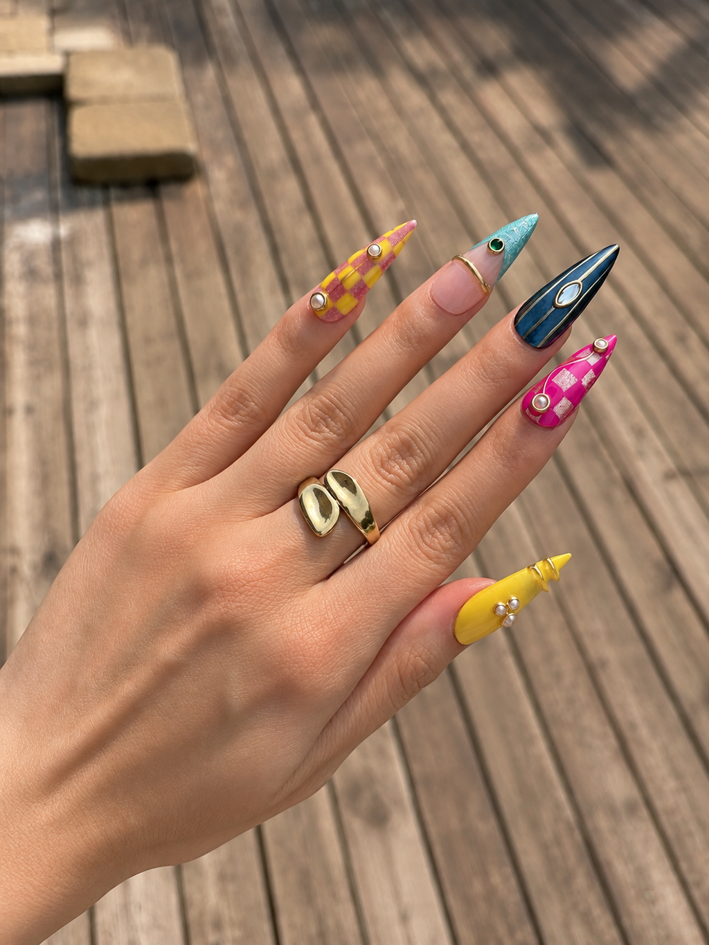 Luxury handmade press-on nails worn on a hand, showcasing vibrant colors, glossy finish, pearls, and elegant gold detailing.