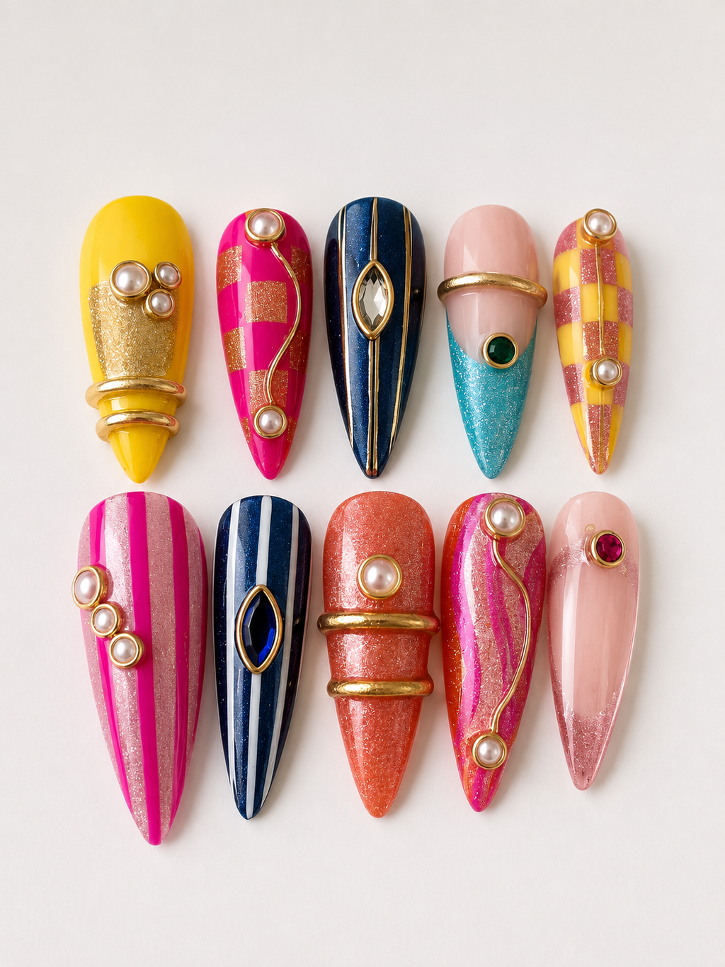 Luxury handmade colorful gel press-on nails with gold metallic details, pearls, gemstones, and artistic modern designs on a white background